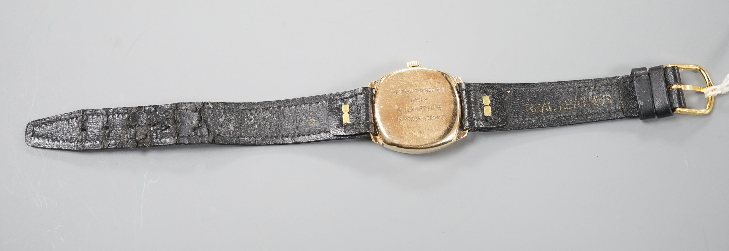 A gentleman's 9ct. gold wristwatch by Garrard in cushion case, silvered dial, baton and Roman numerals, Swiss 16 jewel movement, c.1957 inscription to back, black leather strap, cased diameter, 30mm, gross 24 grams.